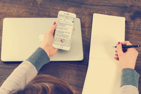 A woman looking at a phone and writing a list