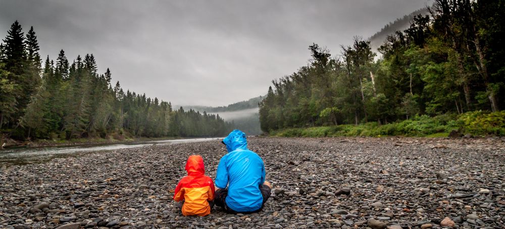 A father and sun sit on a river bank outside of Whistler