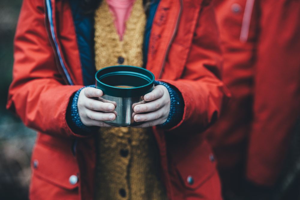 A woman in rain jacket holding a cup of hot chocolate